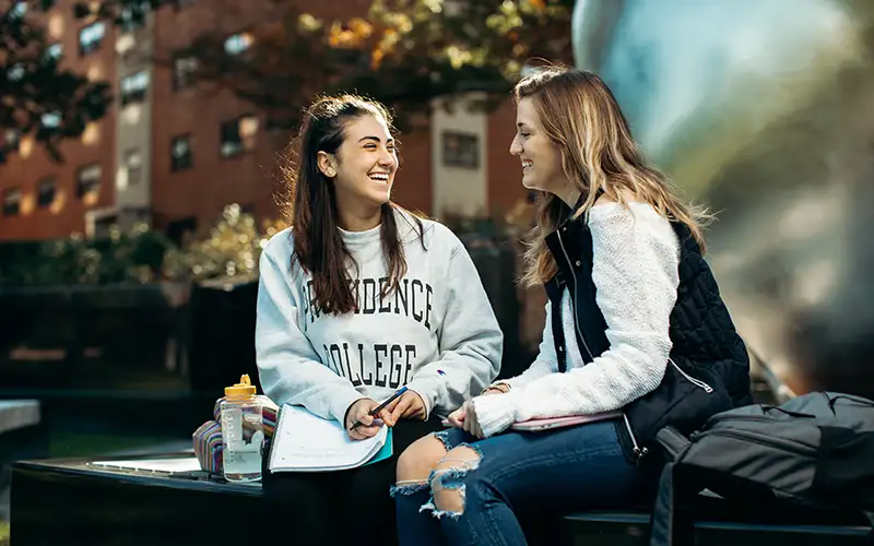 two students talking to each other sitting in front of the calabria plaza