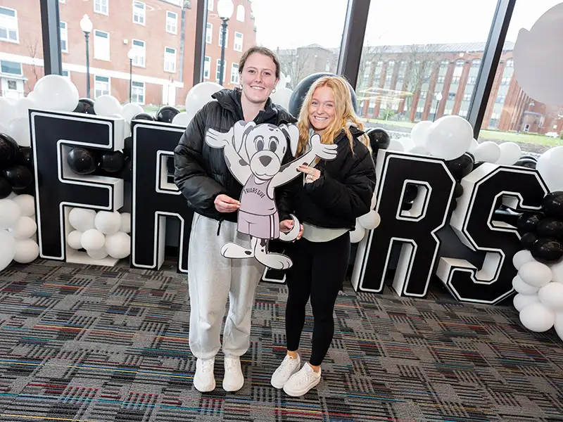 students holding huxley cutout in front of Friars sign