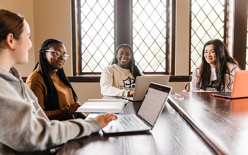 Group of four female students in a classroom talking