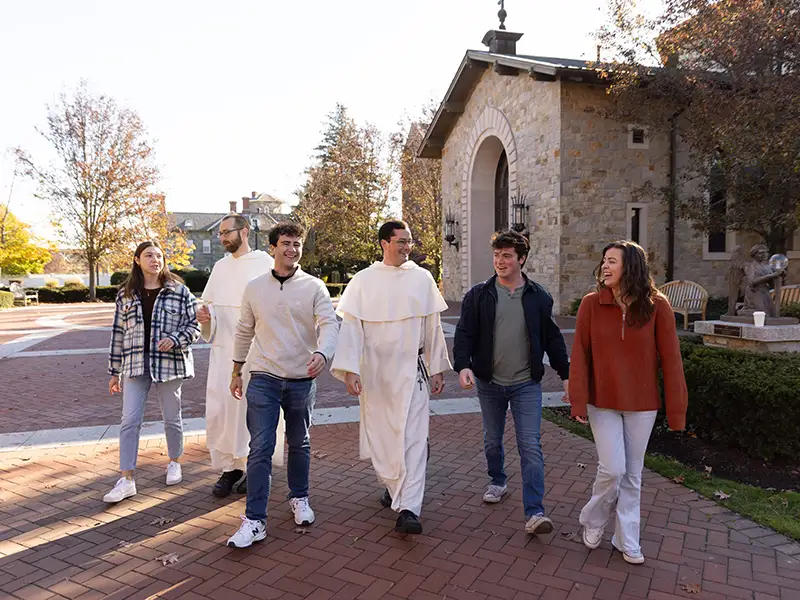 students and priest walking outside chapel