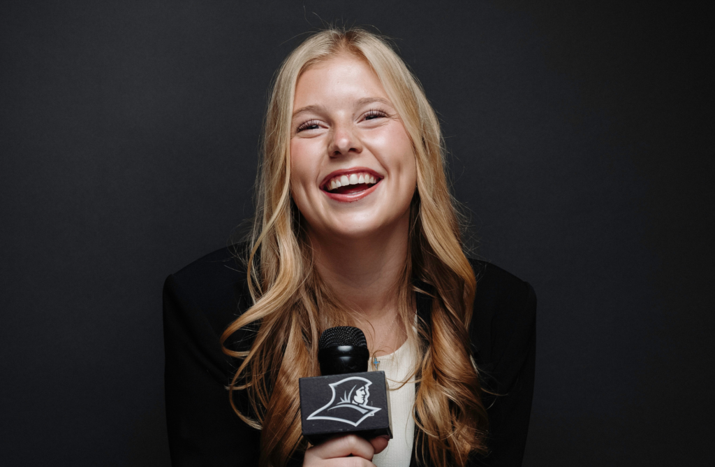 A female student poses with a Friars microphone for a portrait