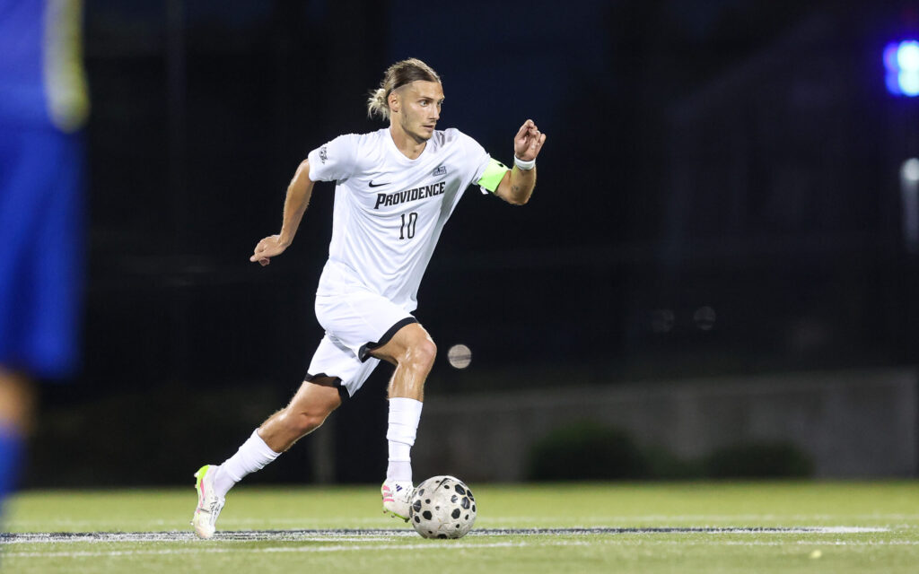 A Friars soccer player dribbles the ball on turf