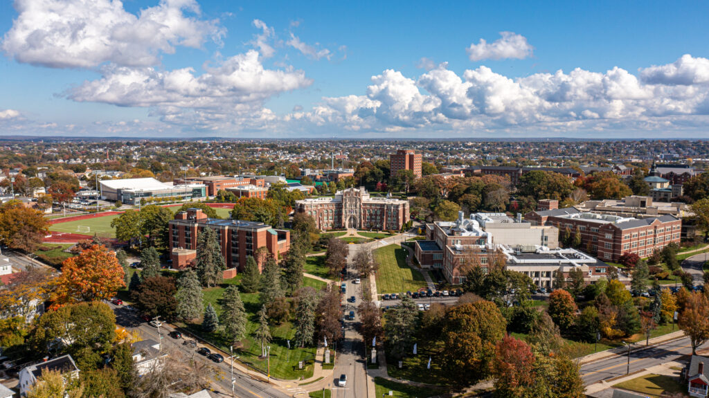 Aerial shot of PC's campus with Harkins Hall in the foreground and the Providence skyline behind