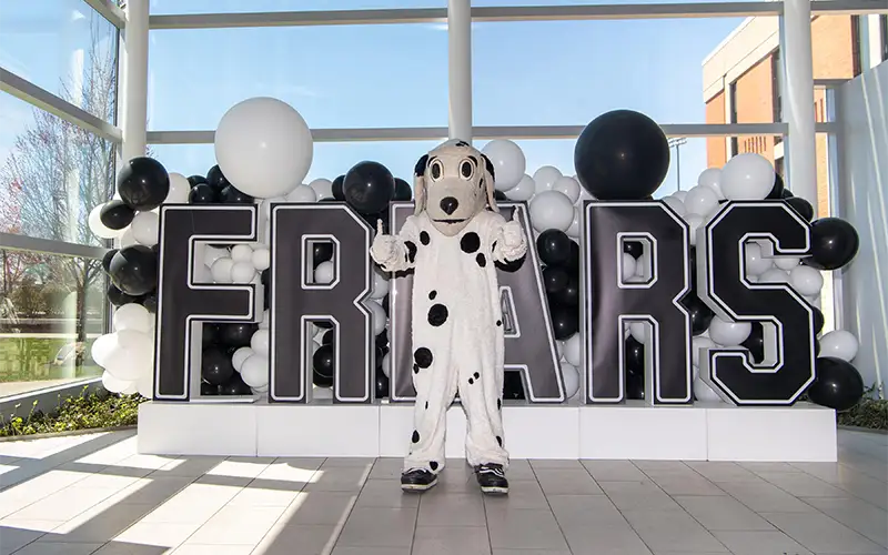 huxley mascot with friars sign behind him